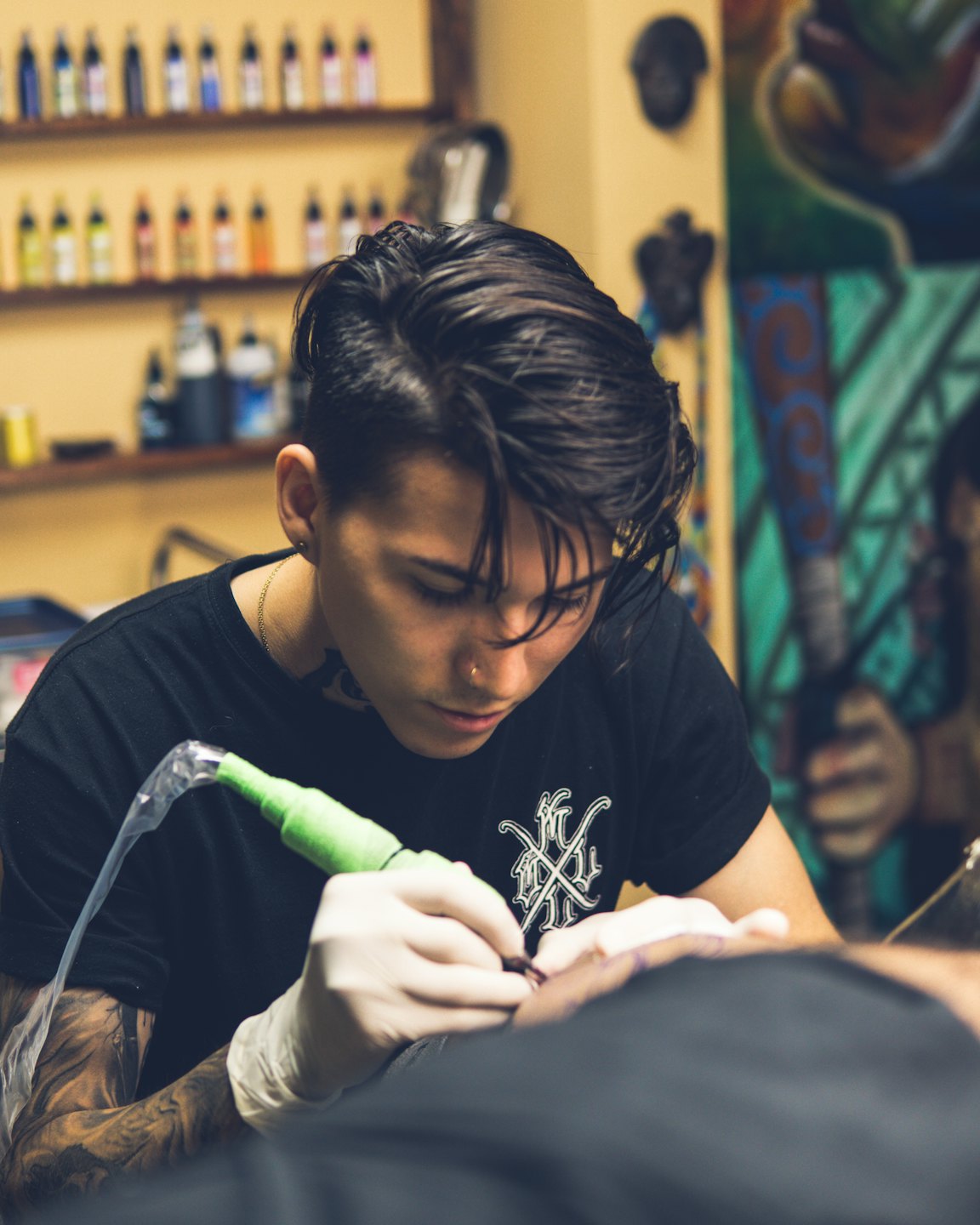 Tattoo artist uses a green machine on a client's arm.